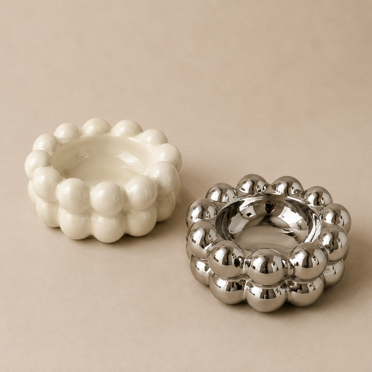 White textured ashtray and silver metallic ashtray on a beige background