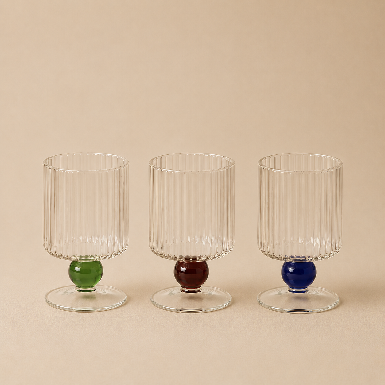 Three transparent glass with colored bases on a beige background