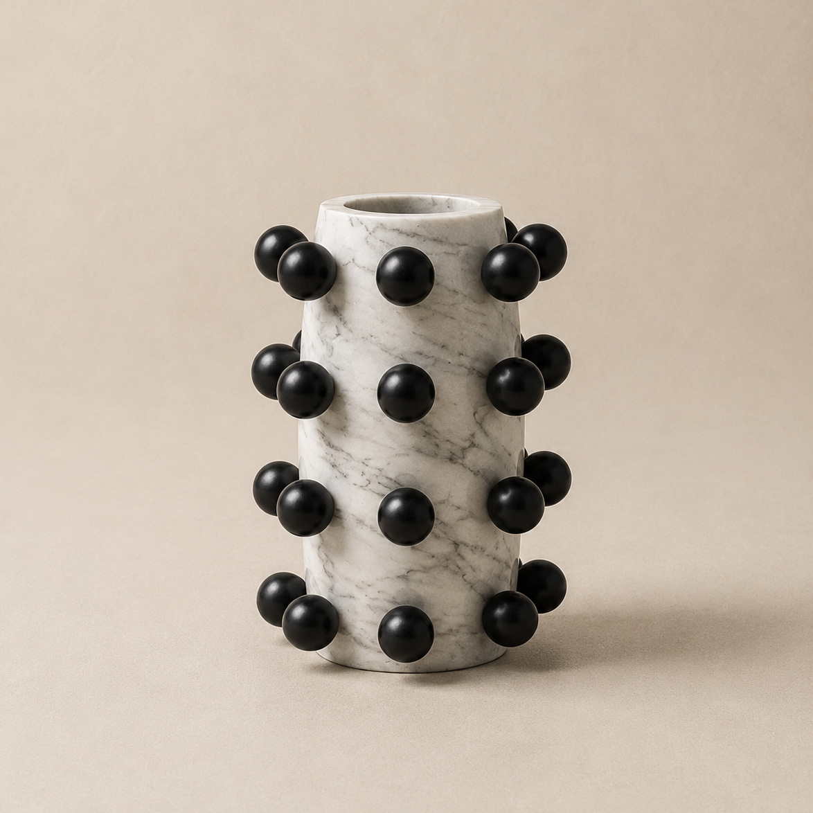 Marble vase with black spherical accents on a beige background
