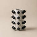 Marble vase with black spherical accents on a beige background