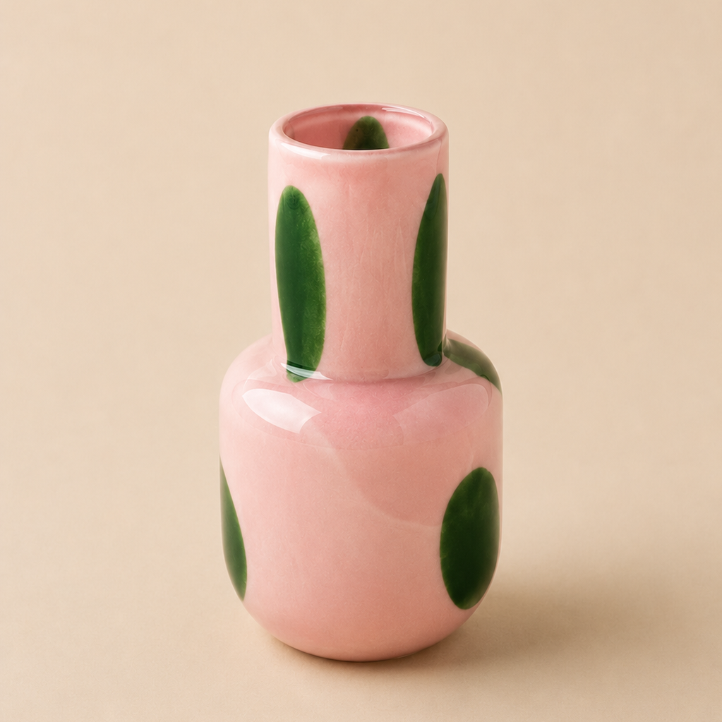 Pink ceramic vase with green polka dots on a beige background